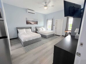 Ein modernes Schlafzimmer mit zwei Betten, einem Deckenventilator, einer Klimaanlage und einem Fernseher.