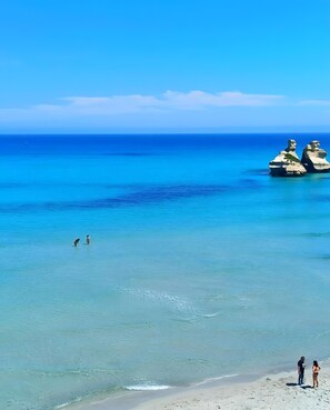 A beach with clear water, two rocky formations, and people on the shore.