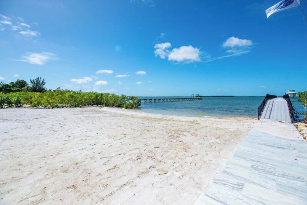 Une plage avec un ciel dégagé, une jetée qui s’avance dans l’eau et une promenade couverte menant à un bâtiment.