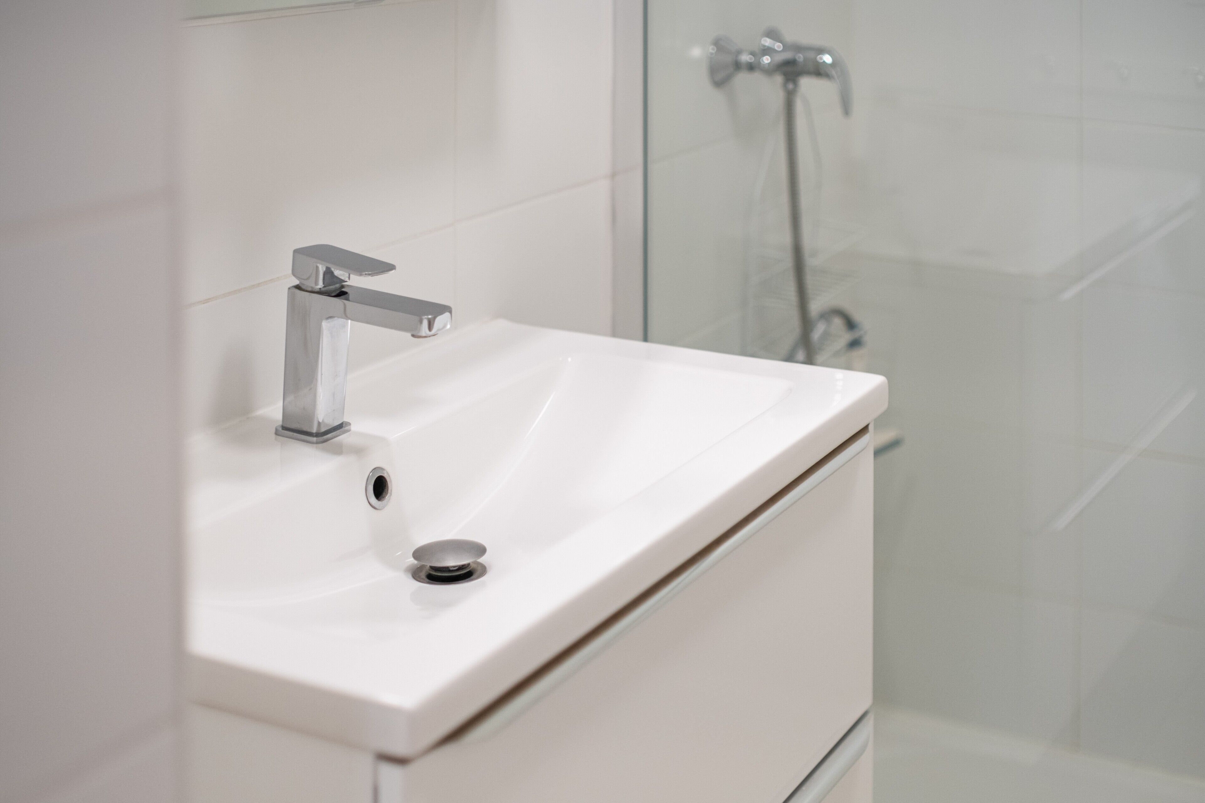 Een badkamer met een wit wastafelmeubel, een chromen kraan en een douchecabine van glas.