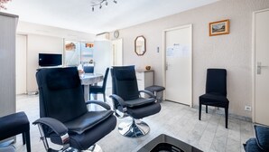 A room with two black chairs, a ceiling fan, a television, and a door with a sign. - 3-Star Tourist Apartment with Sea View, Wi-Fi, and Air Conditioning (Golfe-Juan)