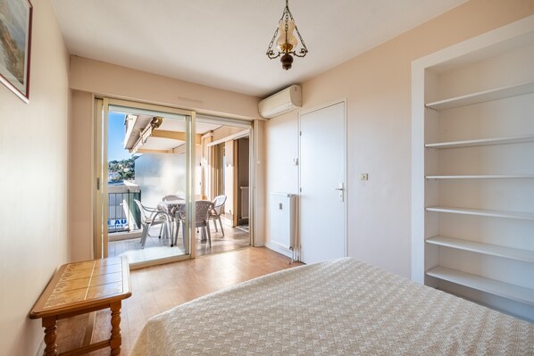 A bedroom with a bed, a wooden table, a radiator, and a sliding glass door leading to a balcony.