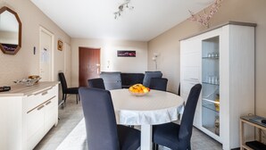 A dining area with a round table, chairs, a fruit bowl, a cabinet with glass doors, and a mirror on the wall. - 3-Star Tourist Apartment with Sea View, Wi-Fi, and Air Conditioning (Golfe-Juan)