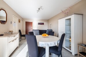 Un coin repas avec une table ronde, des chaises, un panier de fruits, un meuble avec des portes en verre et un miroir au mur.