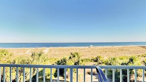 A beach view with a clear sky, palm trees, and a distant shoreline. - Ocean Song 323 | Incredible View, Two Pools (Tybee Island)
