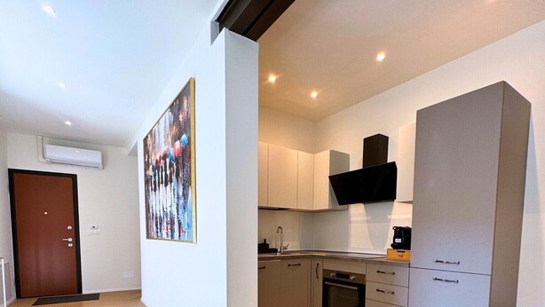 A modern kitchen with white cabinets, a black range hood, and a wooden floor.