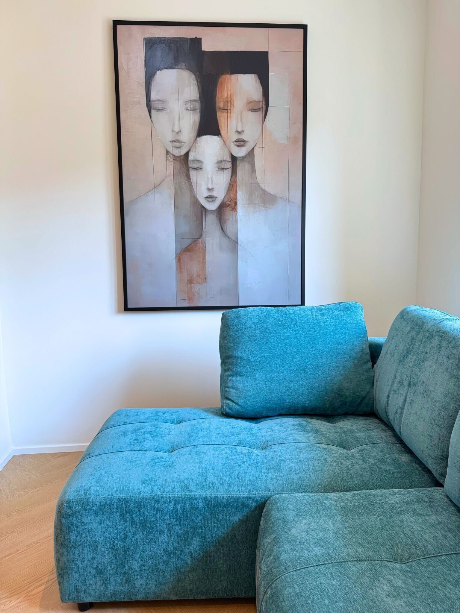 Een smaragdgroene bank in een kamer met een ingelijst abstract schilderij aan de muur.