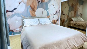 A bedroom with a large bed, a smaller bed, and a floral wall mural.