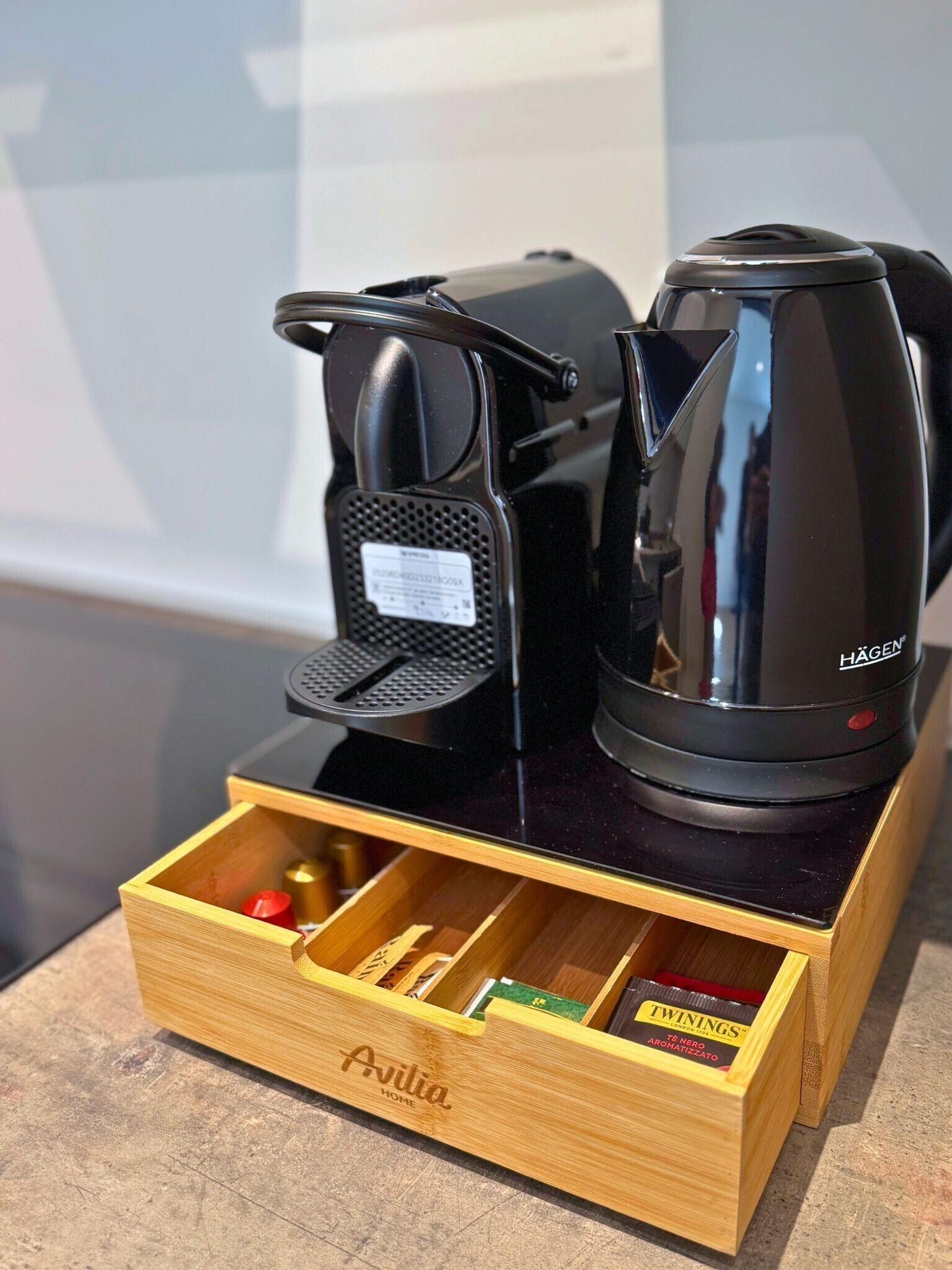 A coffee maker and a kettle on a wooden tray with a drawer containing tea bags.