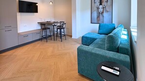 A modern living room with a sofa, a dining area with chairs, a TV mounted on the wall, and a painting.