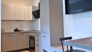 A modern kitchen with white cabinets, a built-in oven, a sink, and a dining area with a table and chairs.