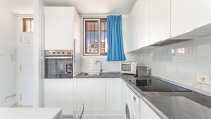 Une cuisine compacte équipée d’un four encastré, d’un four à micro-ondes, d’un lave-linge et d’une fenêtre agrémentée d’un rideau bleu.