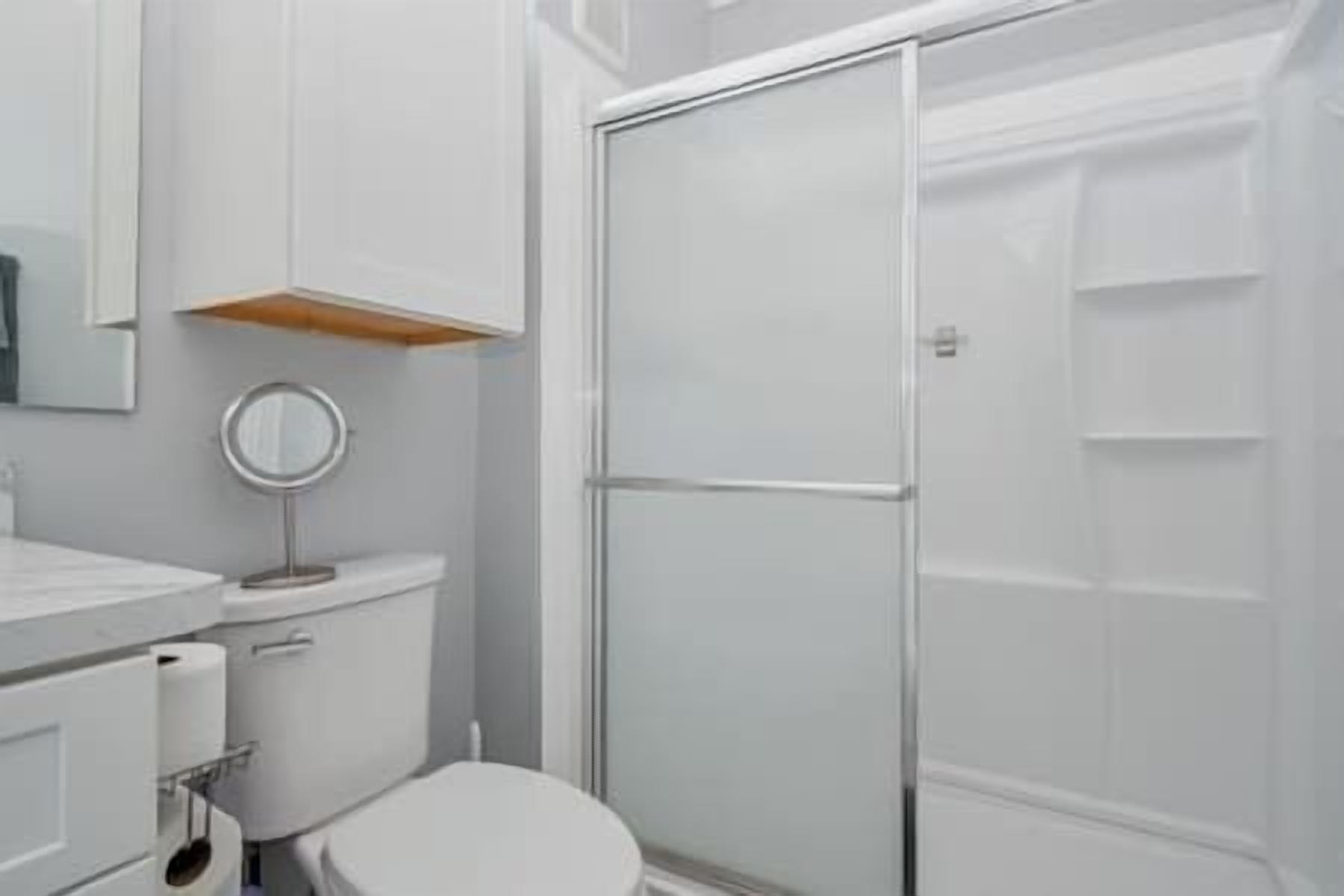 A bathroom with a toilet, a mirror, a shower enclosure, and a sink.
