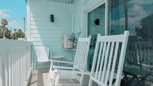 A balcony with white chairs and a table, a sliding glass door, and a small air conditioning unit. - Unit 126 Beautiful Cedar key (Cedar Key)