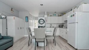 A modern kitchen with white cabinetry, a dining area with two chairs, a washing machine, and a refrigerator. - Unit 126 Beautiful Cedar key (Cedar Key)