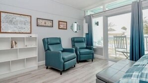 A room with two teal armchairs, a white shelving unit, and a large window with curtains. - Unit 126 Beautiful Cedar key (Cedar Key)
