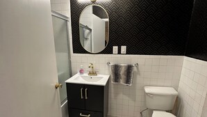 Une petite salle de bain avec un lavabo blanc, un meuble-lavabo noir, des toilettes et un miroir avec un éclairage au-dessus.