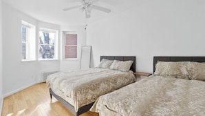 Une chambre avec deux lits, un ventilateur de plafond et de grandes fenêtres.