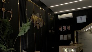A modern hotel lobby with a black and gold color scheme, featuring a reception desk, two armchairs, a small table with a vase, and a decorative wall piece. - Jerash Hotel (Jerash)