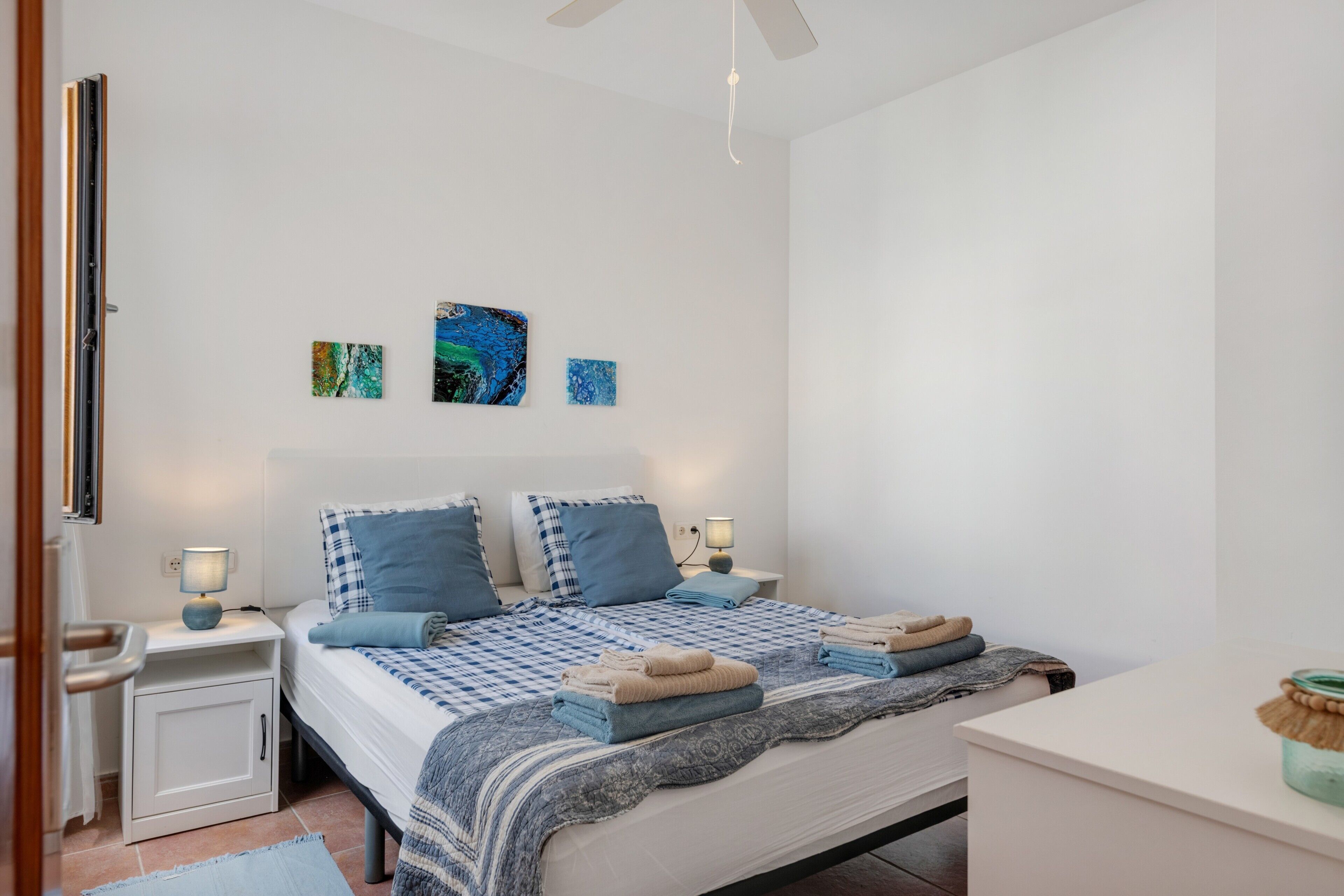Un dormitorio con cama, mesitas de noche, un ventilador de techo y decoración en la pared.