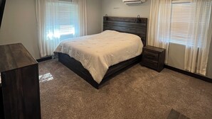 Un dormitorio con una cama, ventilador de techo, aire acondicionado y una mesita de noche.