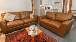 A living room with two brown leather sofas, a coffee table with a book and a teapot, and a red patterned rug. - Llainorfa (New Quay)