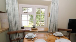 A dining table set for four with white plates, glasses, and cutlery, positioned in front of a window with a view of greenery. - Llainorfa (New Quay)