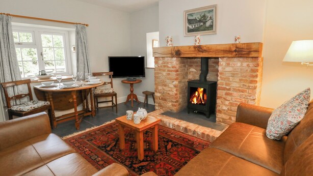 A cozy living room with a fireplace, leather sofas, a dining area with a table set for four, and a television. - Llainorfa (New Quay)