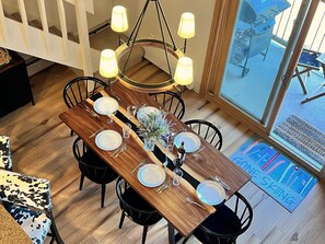 A dining area with a wooden table set for six, surrounded by black chairs, and a chandelier overhead.