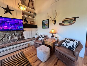 A cozy living room with a stone fireplace, leather sofas, a flat-screen TV, and decorative antlers on the wall.
