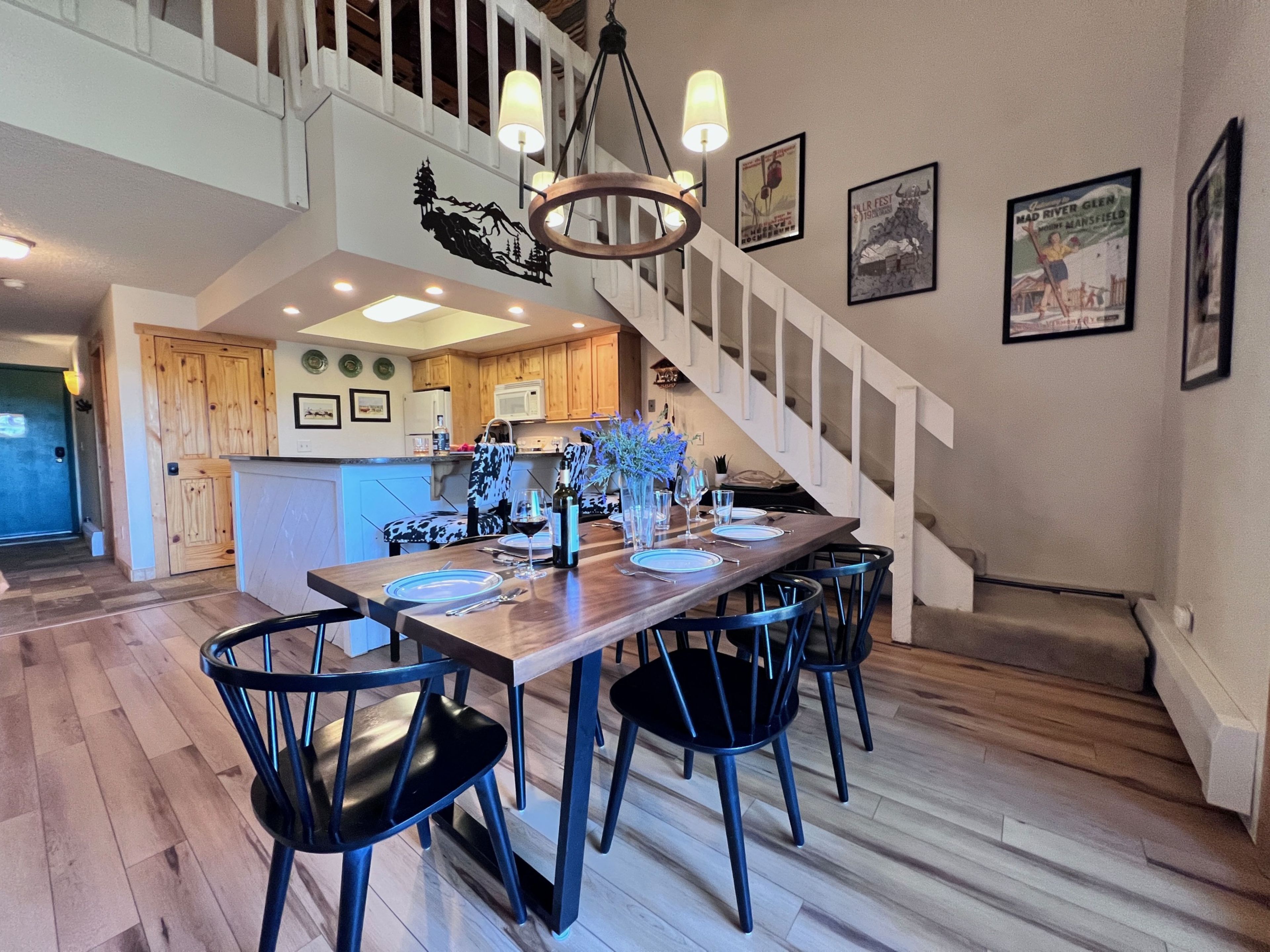 Un comedor con mesa y sillas de madera, una escalera y una cocina al fondo.