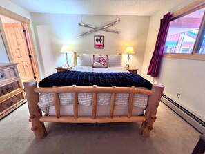 A bed with a wooden frame, two bedside lamps, a wall-mounted sign, and a window with curtains.