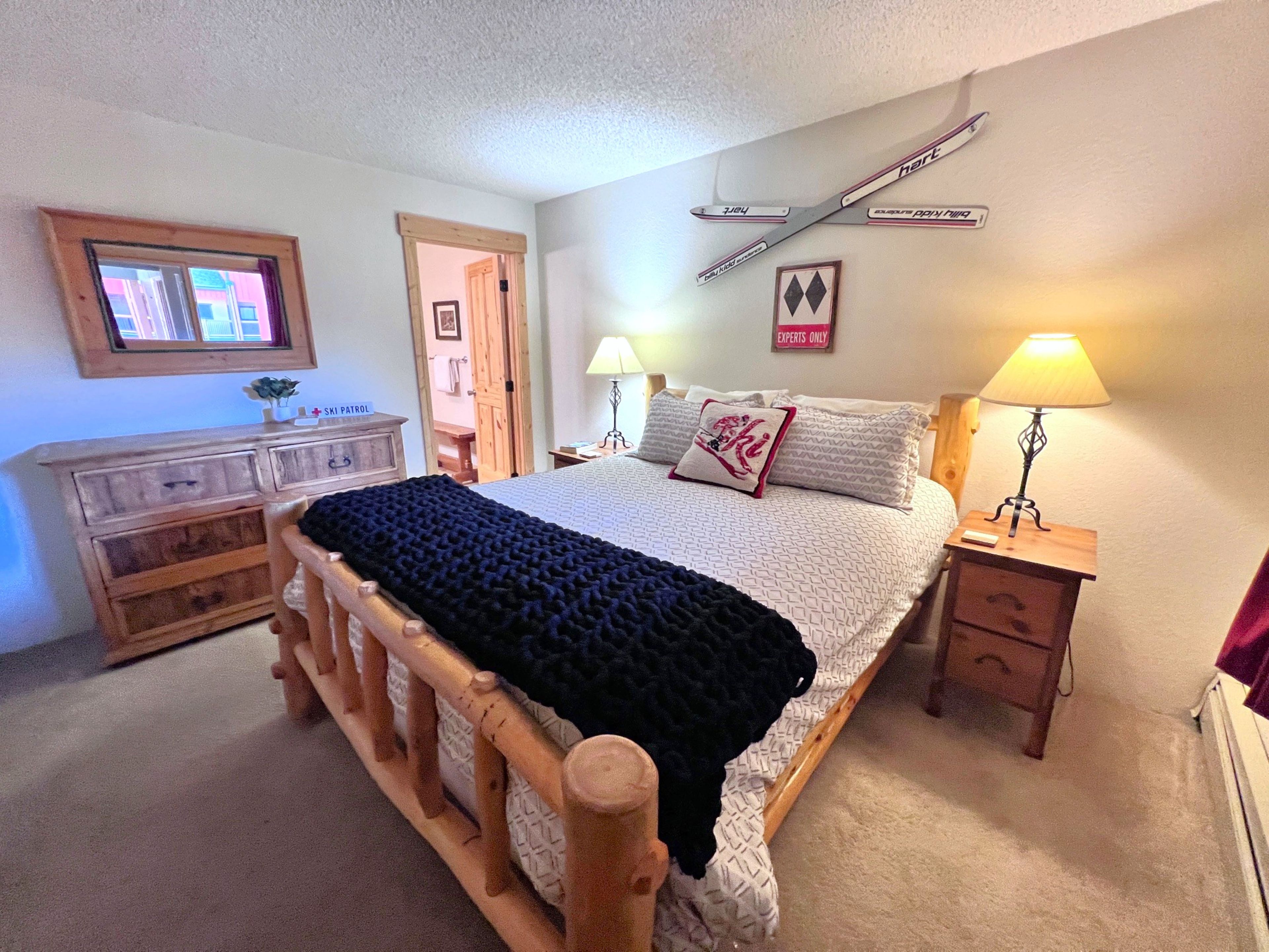 A bedroom with a wooden bed, a desk, a chair, a lamp, and a ski patrol sign on the wall.