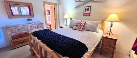 A bedroom with a wooden bed, a desk, a chair, a lamp, and a ski patrol sign on the wall.