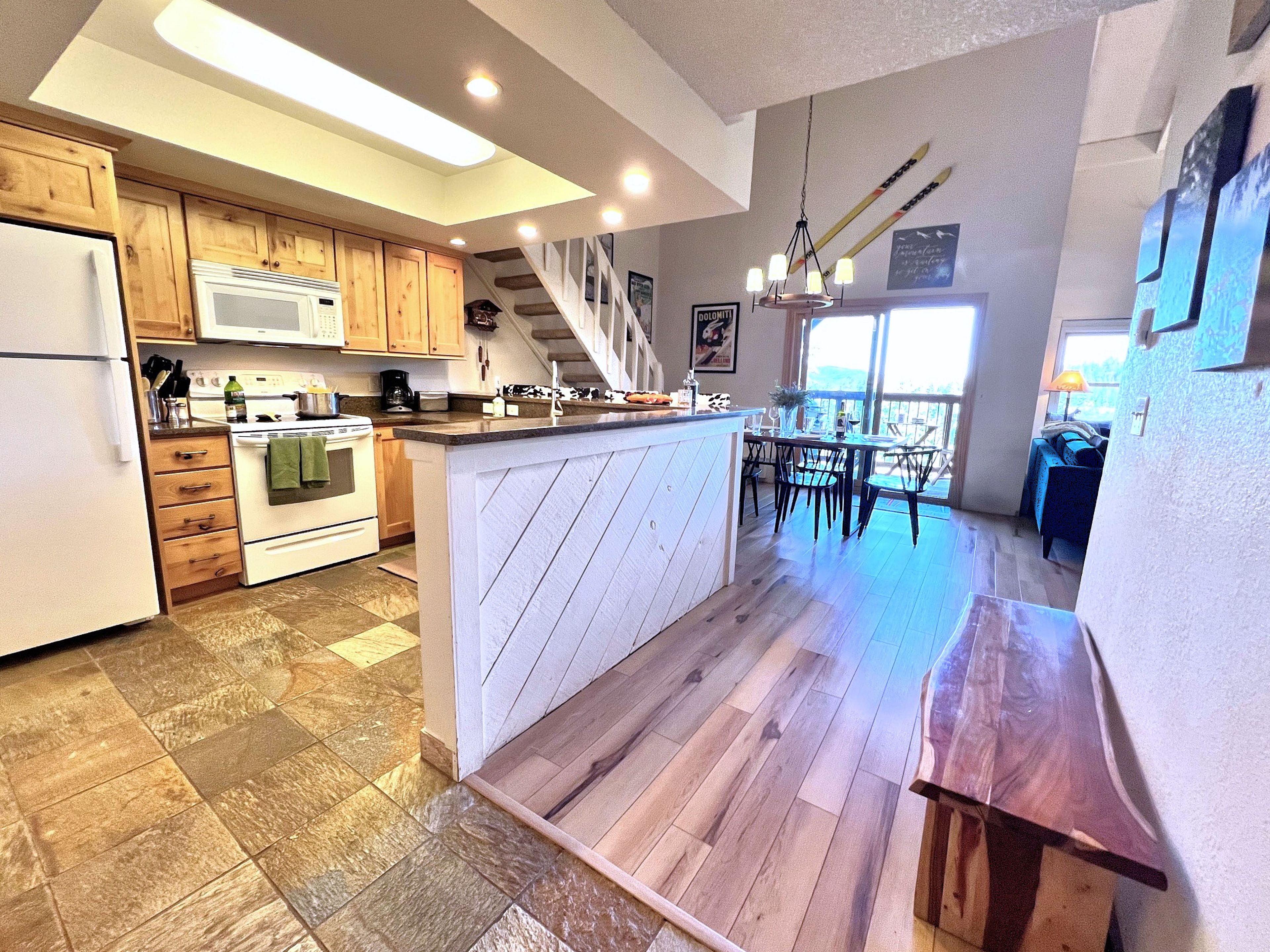 A kitchen with wooden cabinets, a white refrigerator, a stove, and a dining area with a table and chairs.