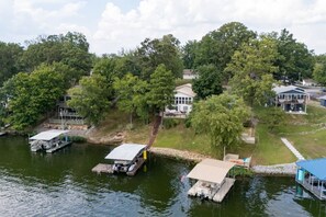 A lakeside property with docked boats, a covered boat ramp, and houses with large windows and a porch. - Waterfront Views, Kayaks, Pets w/ Fee (Creal Springs)