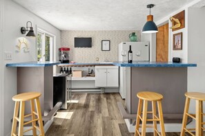 A compact kitchen with a central island, bar stools, a refrigerator, and a television. - Waterfront Views, Kayaks, Pets w/ Fee (Creal Springs)