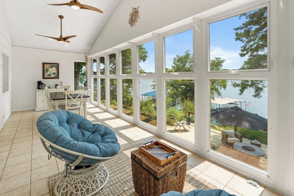 A spacious room with large windows, a blue bean bag chair, a small table, and a view of a lake. - Waterfront Views, Kayaks, Pets w/ Fee (Creal Springs)