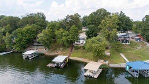 A lakeside property with docked boats, a covered dock, and a house with a porch. - Wild Sun Retreat- Waterfront, firepit, Kayak, lily pad, pet friendly with fee (Creal Springs)