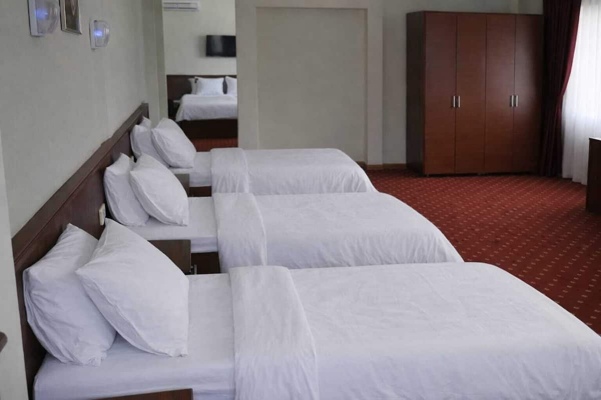 Une chambre d’hôtel avec trois lits simples, une armoire, un téléviseur et un sol recouvert d’une moquette rouge.
