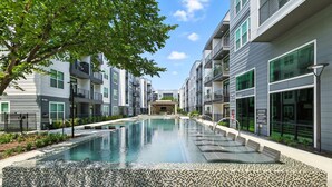 A modern apartment building with a central courtyard pool, balconies, and a clear sky.