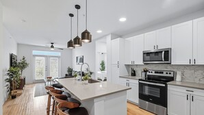 A modern kitchen with white cabinets, a stainless steel oven, a microwave, and a bar area with stools.