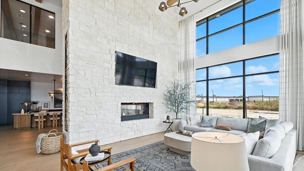 A spacious living area with a white brick wall, a fireplace, and a large window offering a view of the outdoors.