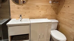 A compact bathroom with a wooden wall, a white sink, a toilet, and a mirror. - COSY STUDIO IN A QUIET LOCATION. NEAR A TUBE STATION. (Pinner)