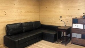 A wooden-paneled room with a black leather sofa, a small table, and a wooden dresser. - COSY STUDIO IN A QUIET LOCATION. NEAR A TUBE STATION. (Pinner)