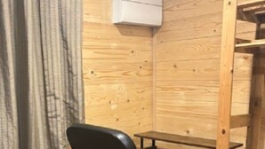 A corner room with a wooden wall, a black office chair, a desk, and a white air conditioning unit. - COSY STUDIO IN A QUIET LOCATION. NEAR A TUBE STATION. (Pinner)
