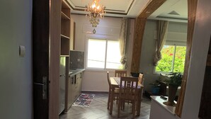 A kitchen with wooden cabinets, a dining table with chairs, a chandelier, and a window with curtains.