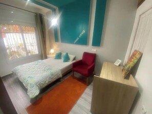 Un dormitorio con una cama, una silla roja, una mesita de madera y un cuadro en la pared.
