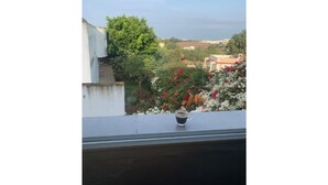A balcony with a cup of coffee, a view of a garden with flowers, and a building in the background. - Spacious one-bedroom apartment close to the sea (Tanger)
