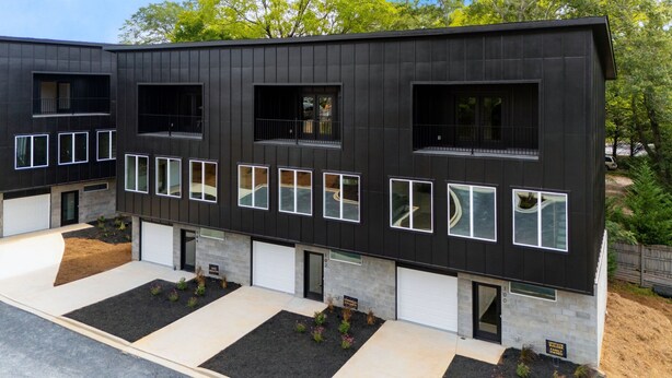 A modern two-story building with a dark exterior, multiple windows, and a driveway with landscaped areas. - Walk to Silos 2BR 2.5BA Townhome + Chef Kitchen Greenville Clemson Area (Easley)